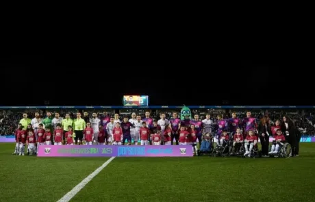 The players of two football teams pose with children, some of them in wheelchairs, behind a banner raising awareness of rare diseases.