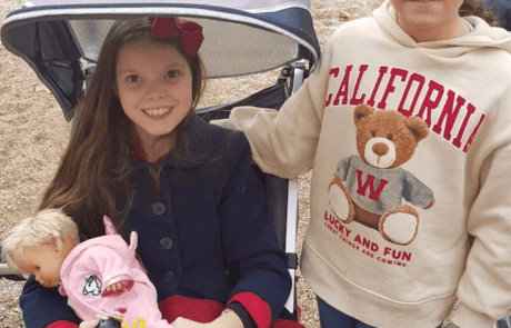Carolina, in her adapted buggy with a doll in her arms, at the park with her best friend Patricia.