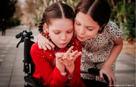 Carolina, in her wheelchair, and her sister Isabel blow a handful of glitter together.
