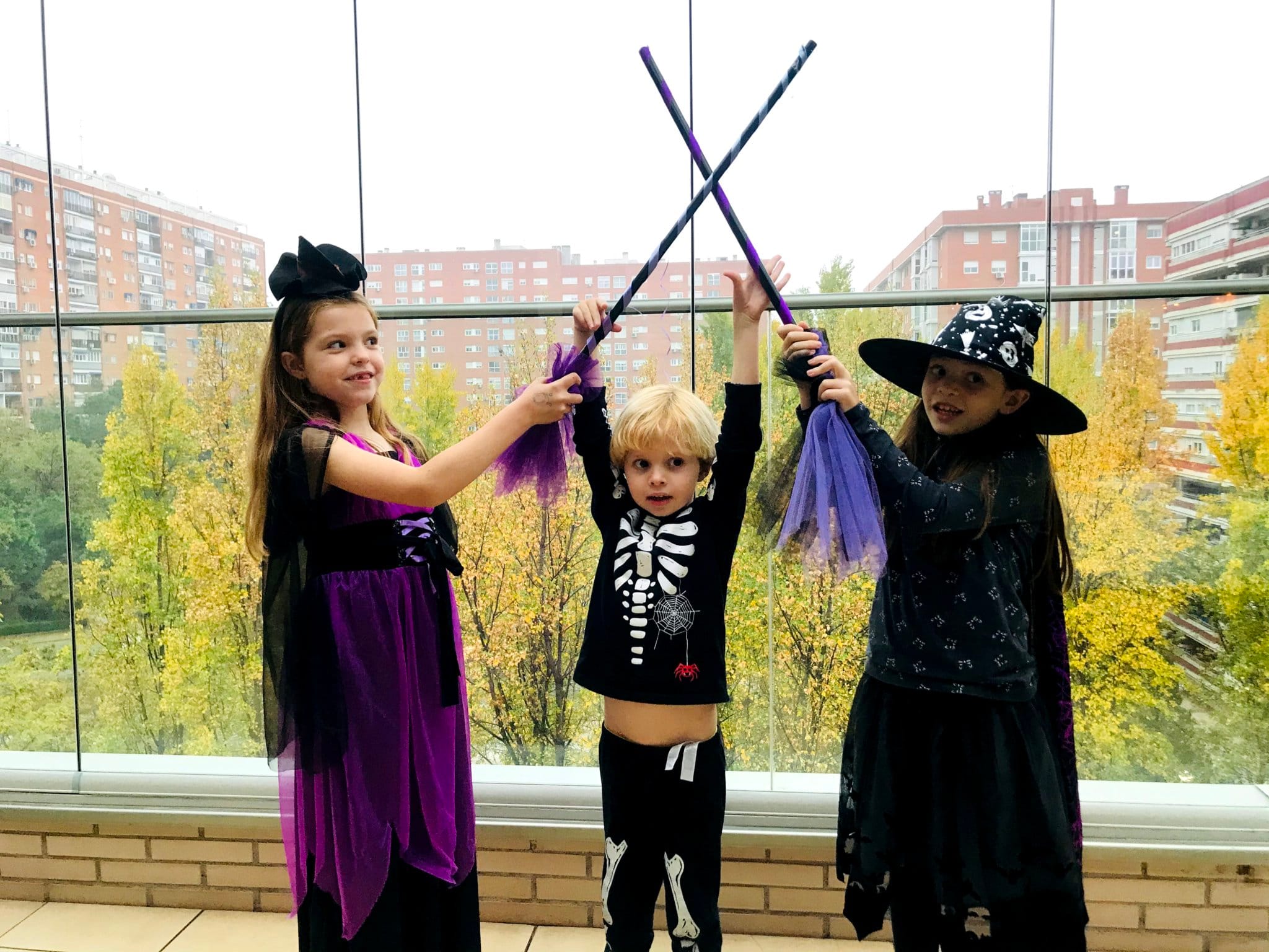 Broomstick games at Carolina Purpurina’s birthday: three children in costume cross their witch brooms.