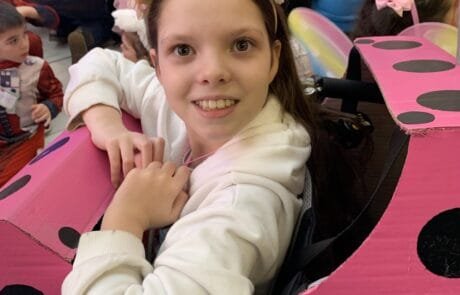 Carolina, wearing a flower crown, smiles inside her pink cardboard bumper car.