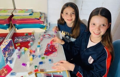 Carolina and a classmate decorate unicorn drawings with glitter at school.