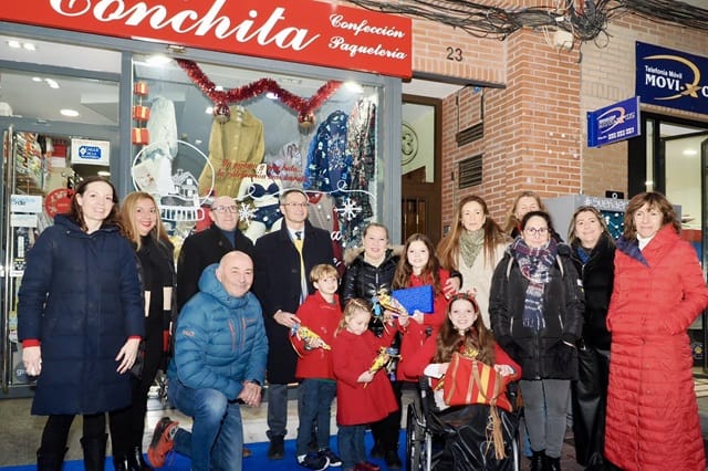 Group photo outside the Conchita shop, with children in red coats and a girl in a wheelchair at the front.