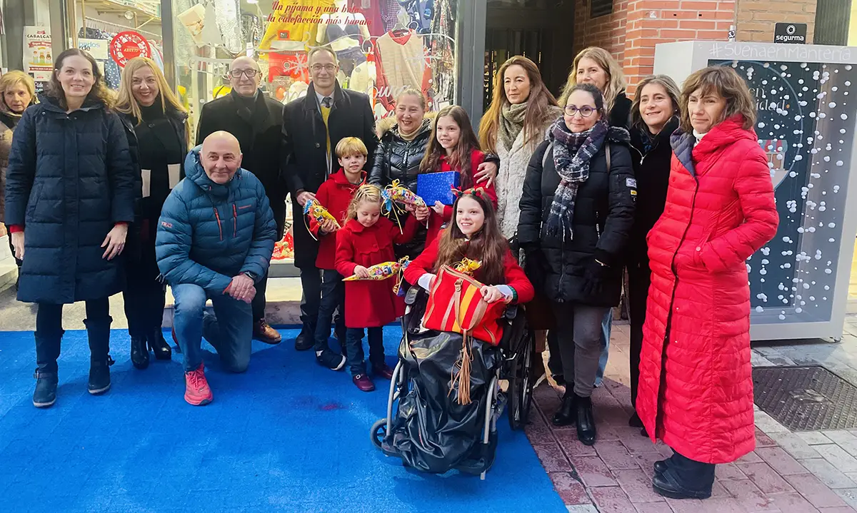 Group photo outside a shop on calle Mantería decorated for Christmas, with a girl in a wheelchair at the centre.