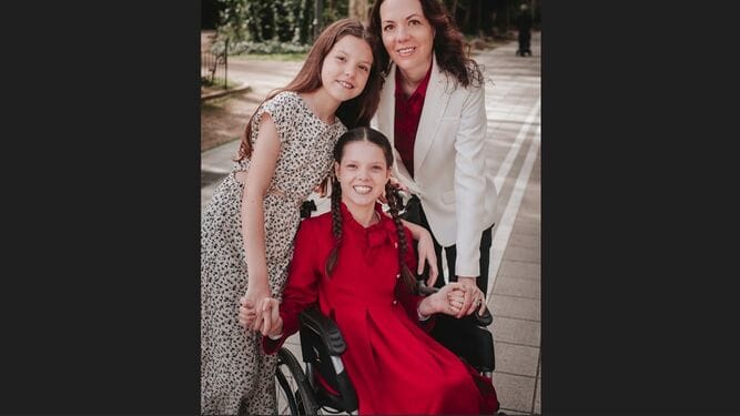 Outdoor portrait: Carolina, in red in her wheelchair, holds hands with her sister and their mother.