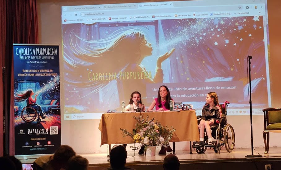 Book talk in a hall: the cover projected on screen, the book’s banner and a girl in a wheelchair beside the table.