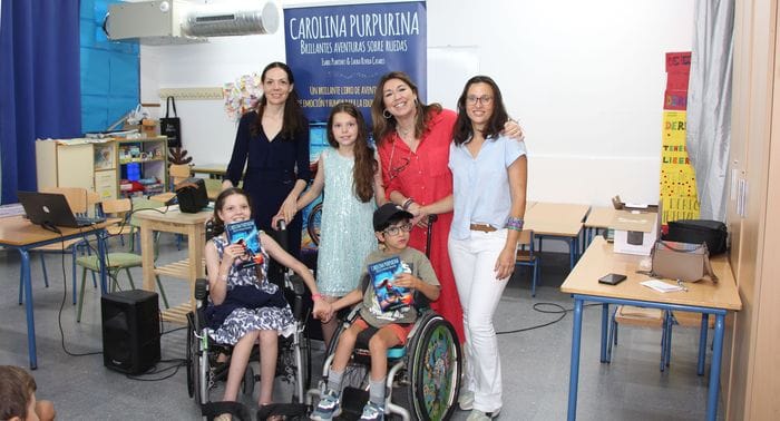 Group photo in a classroom by the book’s banner: three women, a girl and two children in wheelchairs holding copies.