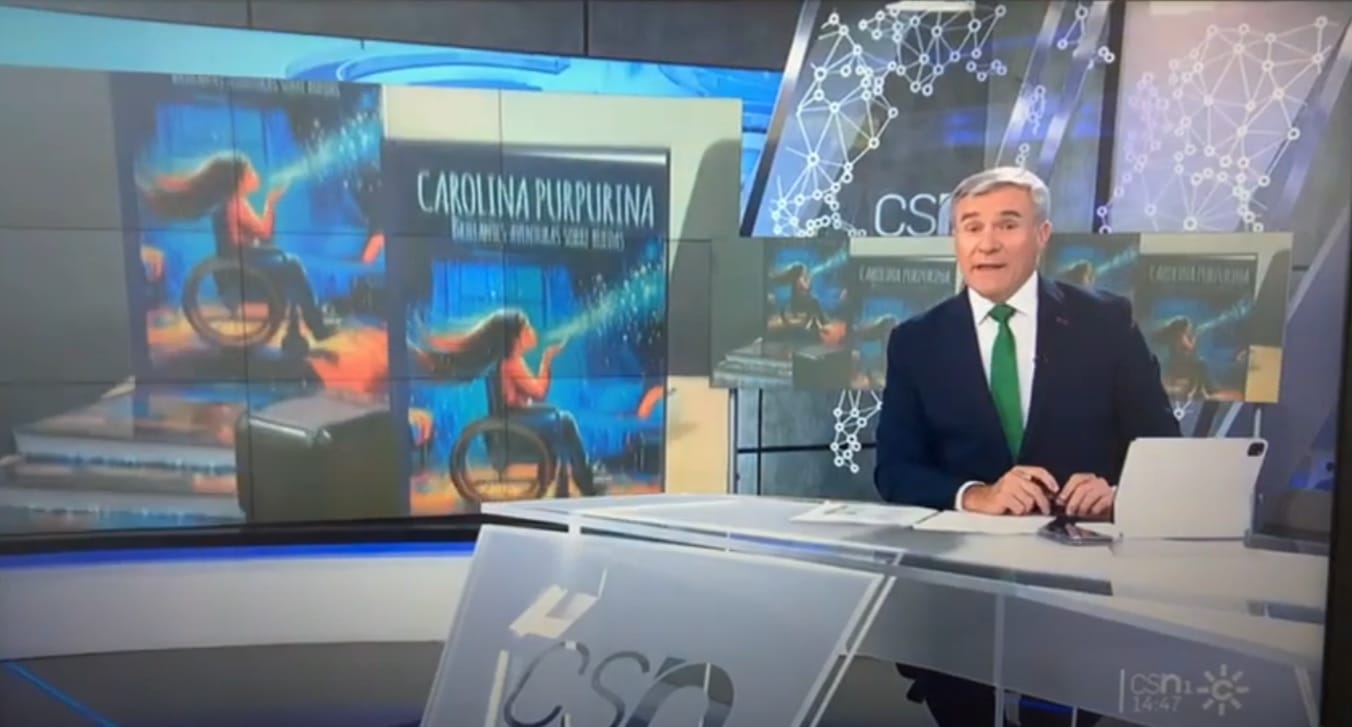 A TV news anchor in the studio, with the cover of “Carolina Purpurina” displayed on the set’s screens.