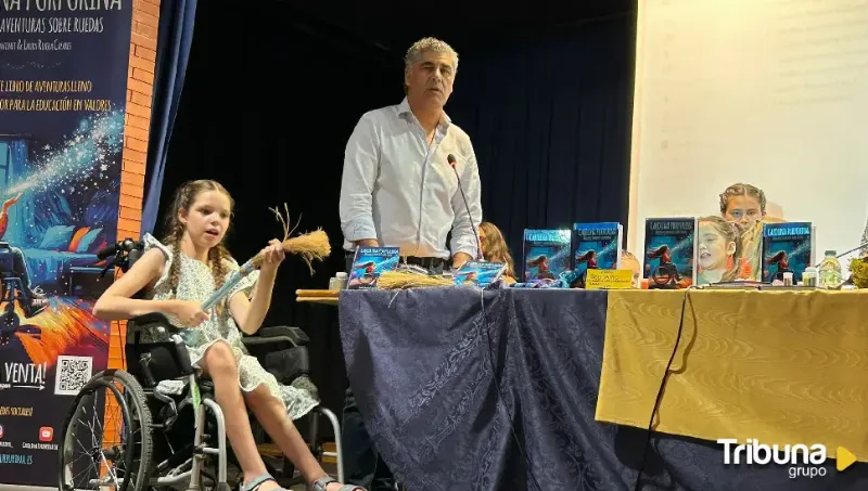 Presentation in a hall: a girl in a wheelchair holds a straw broom beside the table of books on display.