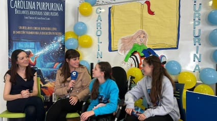 A COPE interview at a school: a reporter with a microphone beside Carolina and two other girls, by the book banner.