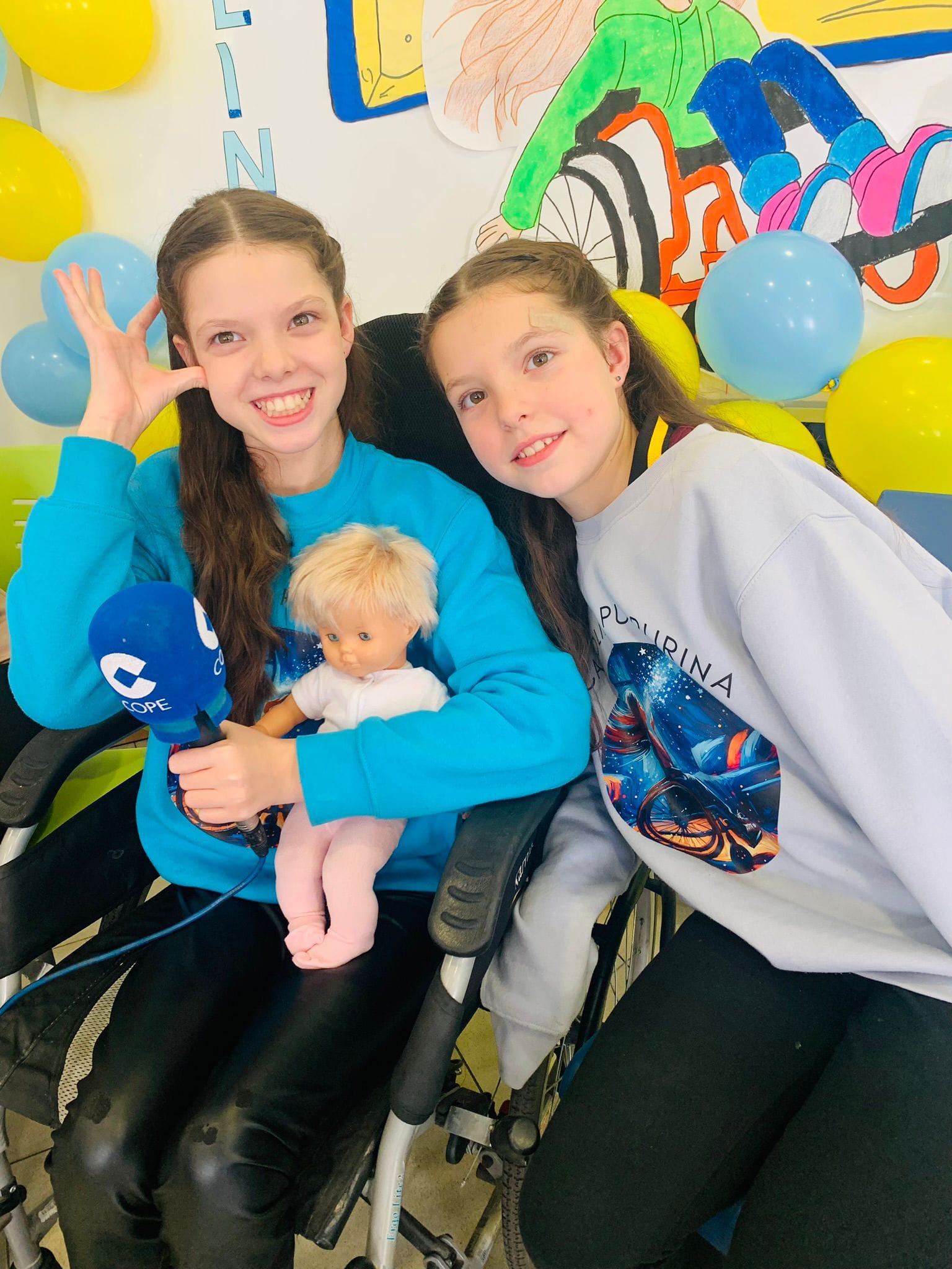 Close-up of Carolina holding the COPE microphone and a doll, beside a girl in a “Carolina Purpurina” sweatshirt.