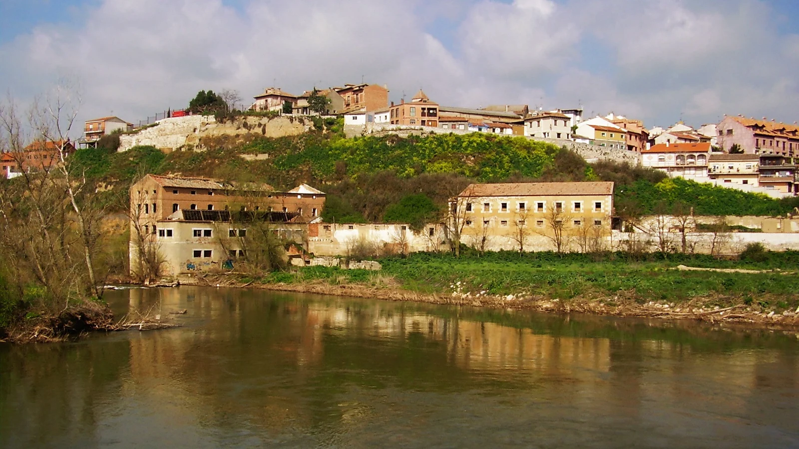 View of a village set on a hillside above a river, with old buildings along the bank.
