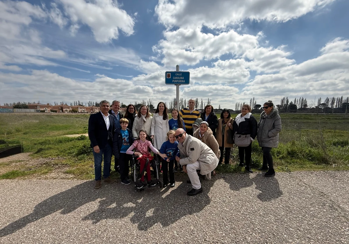 A group poses beneath the Calle Carolina Purpurina street sign, with a girl in a wheelchair at the centre.