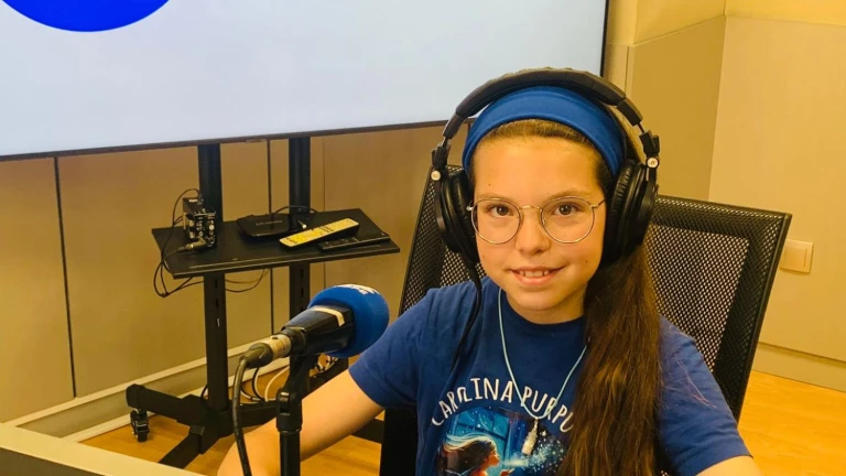 Isabel, wearing headphones and a “Carolina Purpurina” T-shirt, smiles at the microphone in a radio studio.