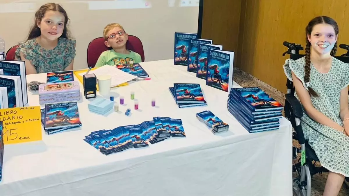 Signing table piled with copies of the book, bookmarks and glitter tubes; on the right, a girl in a wheelchair.