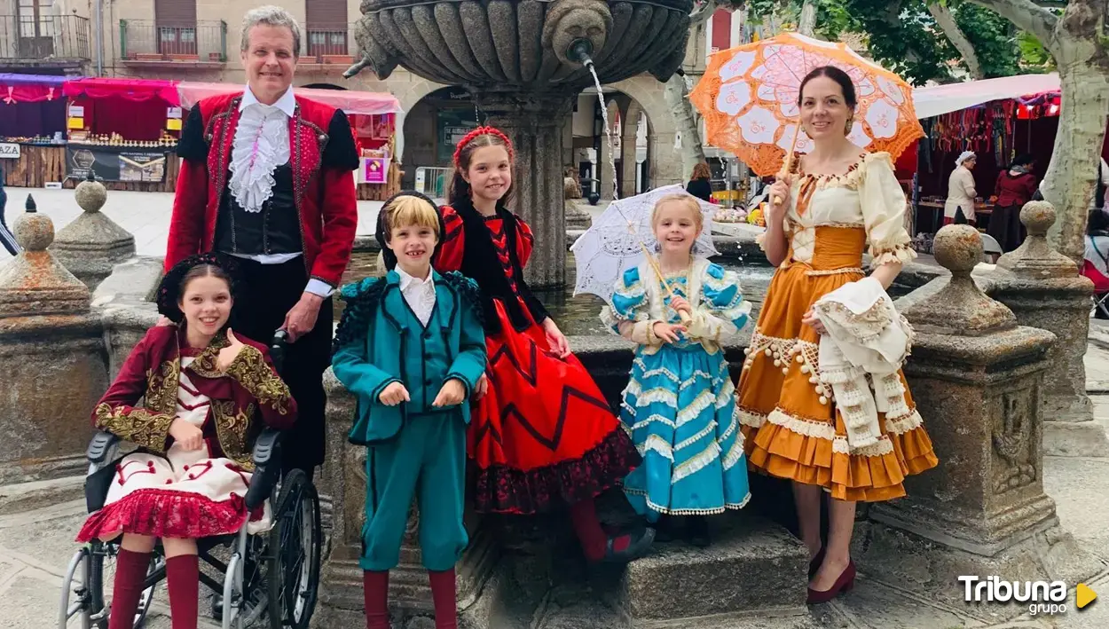By a stone fountain, a group in Goya-era costume with parasols; a girl in a wheelchair gives a thumbs-up.