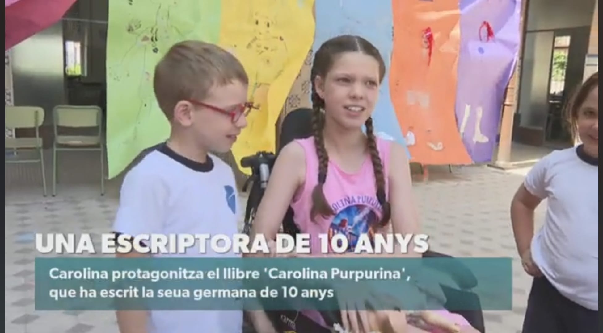 An À Punt news still: Carolina, wearing the book’s T-shirt, talking with a boy in the school playground.