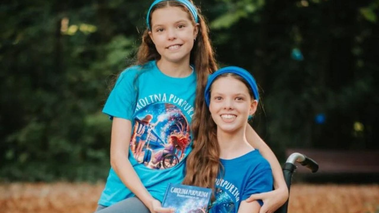 Isabel and Carolina, in Carolina Purpurina T-shirts, hold the book in a park.