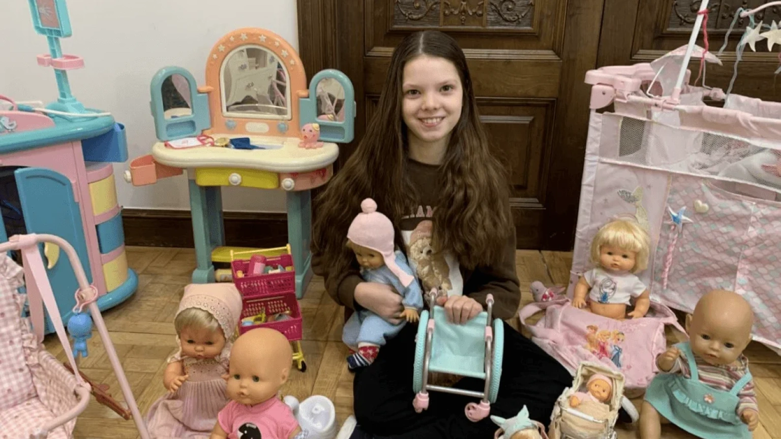 Isabel, sitting on the floor among her dolls, holds a toy wheelchair.