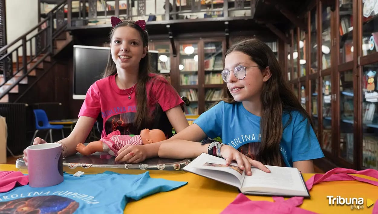 Carolina and Isabel in a library, with the open book, a doll and Carolina Purpurina T-shirts.