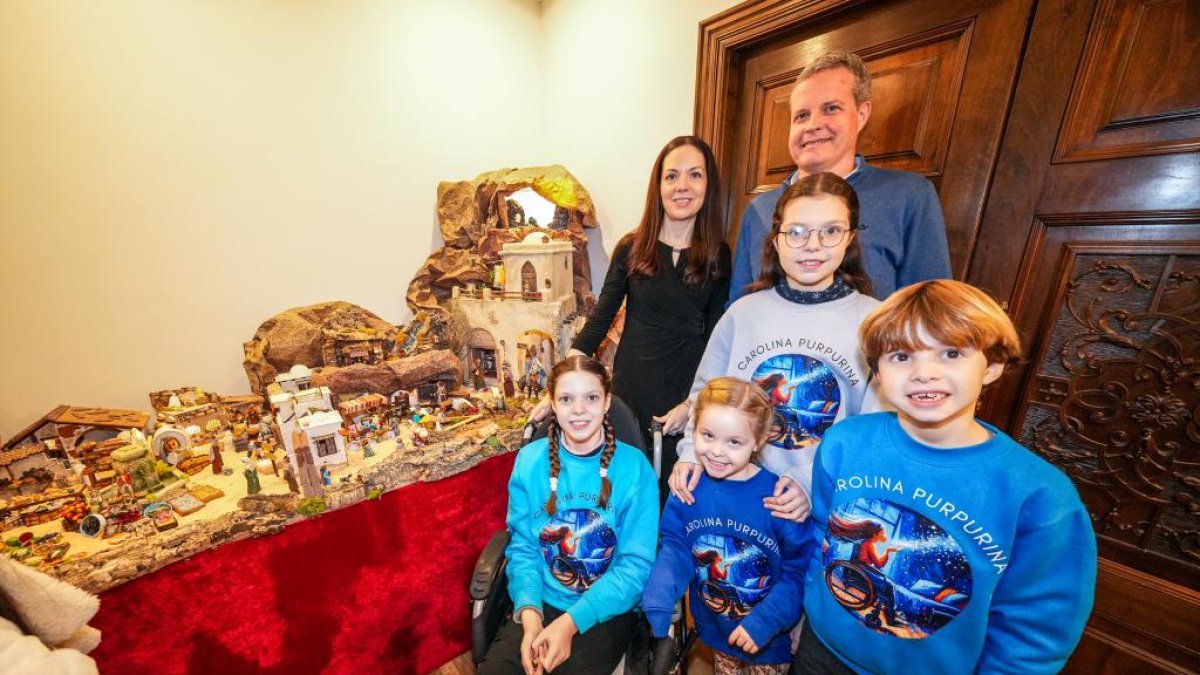 Two adults and four children in Carolina Purpurina sweatshirts beside the nativity scene; in the front row, Carolina in her wheelchair.