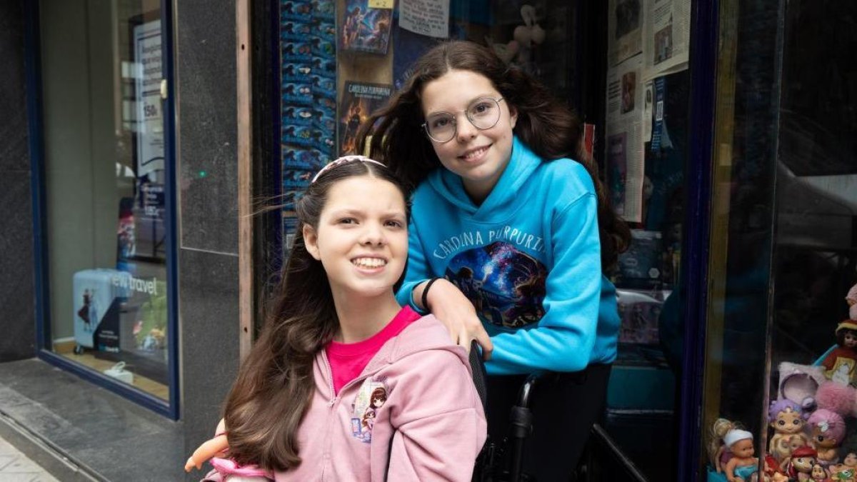 Carolina, in her wheelchair, and Isabel, in a Carolina Purpurina hoodie, pose in front of a shop window displaying the books of the saga.