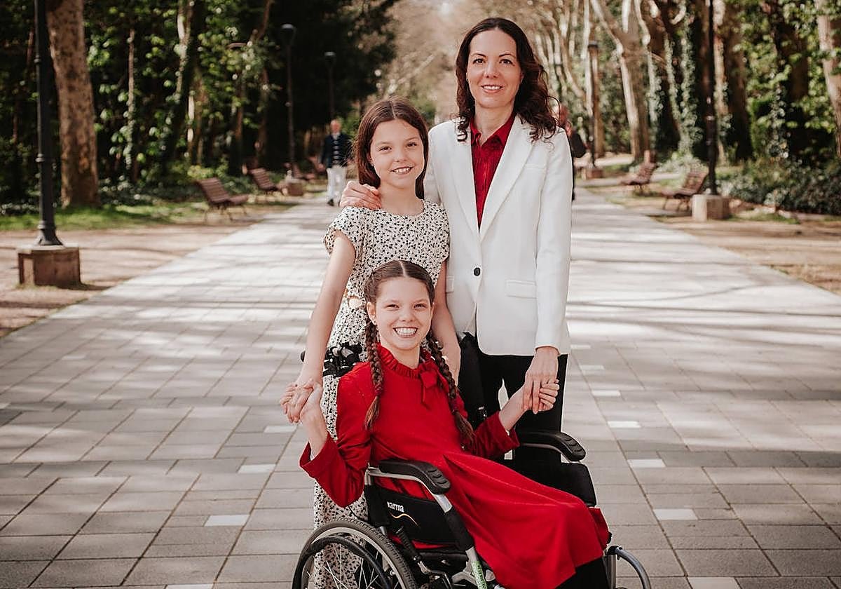 Carolina, in her wheelchair and wearing a red dress, poses with her family on a tree-lined park walkway.