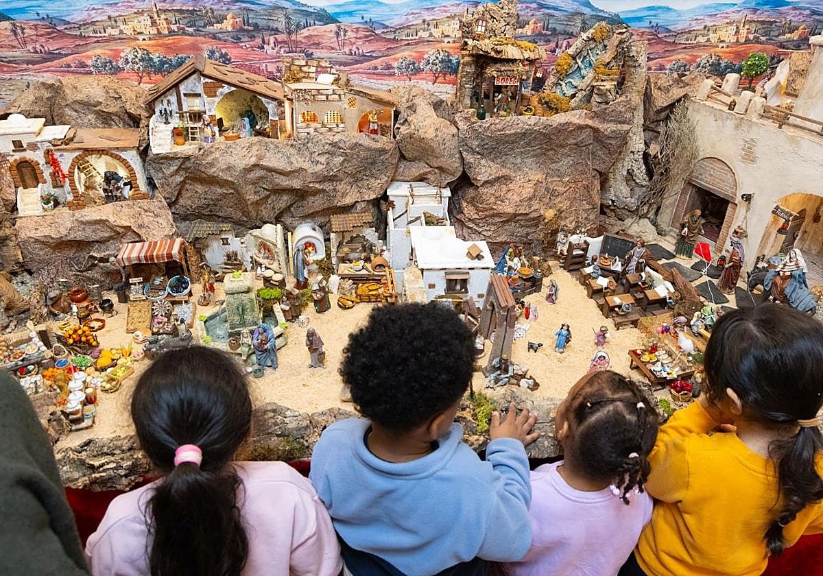 The nativity scene’s first visitors: four children, seen from behind, lean over its landscape of rocks, houses and figures.
