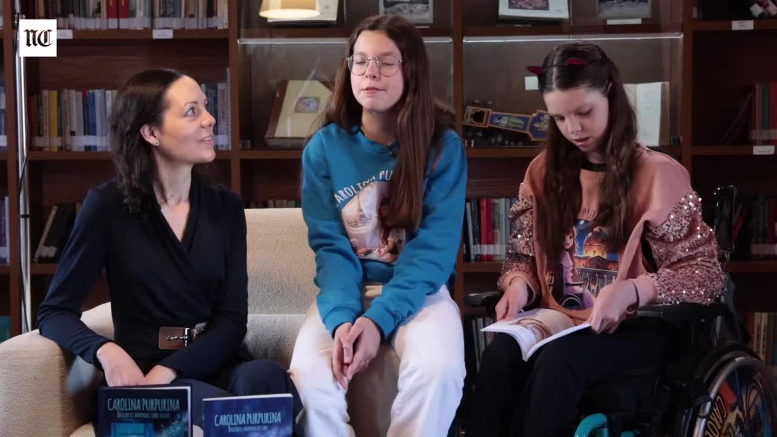 Interview about the third book: Laura and Isabel sit behind two Carolina Purpurina books while Carolina, in her wheelchair, leafs through one.