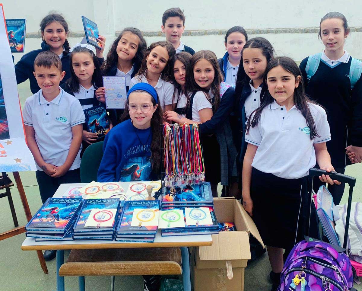 Visit to the Presentación de María school: a girl behind the table of books and bracelets, surrounded by pupils in uniform.